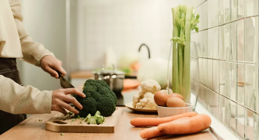 Mãos preparando vegetais frescos em cozinha iluminada, representando o cuidado leve e cotidiano com a alimentação.