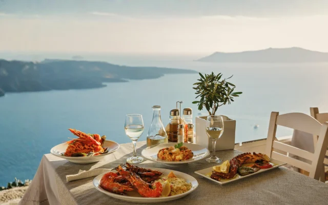 Mesa com refeições mediterrâneas e vista para o mar da Grécia, representando os hábitos alimentares equilibrados e o estilo de vida das Blue Zones.
